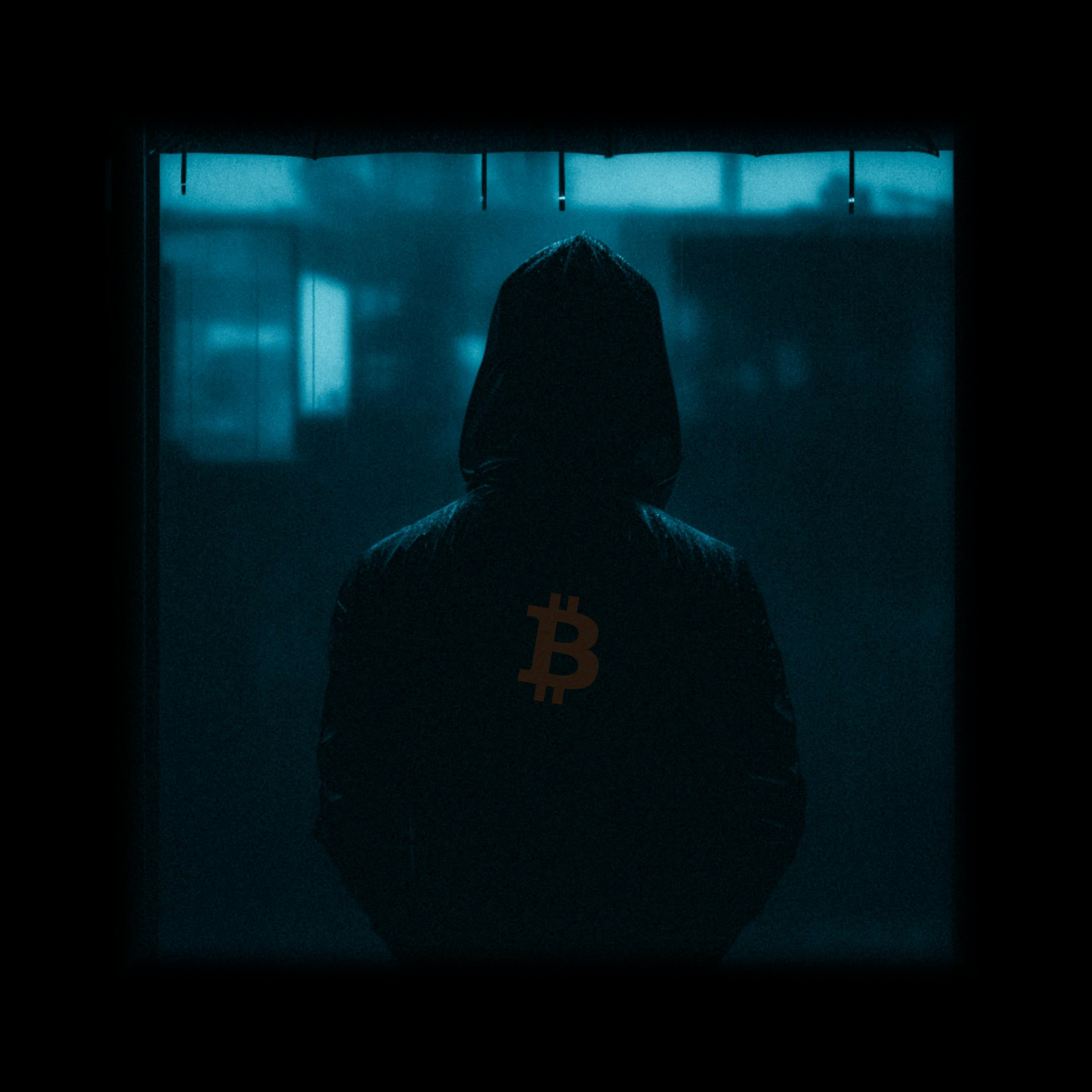 A hooded figure seen from behind with a Bitcoin logo on their back.