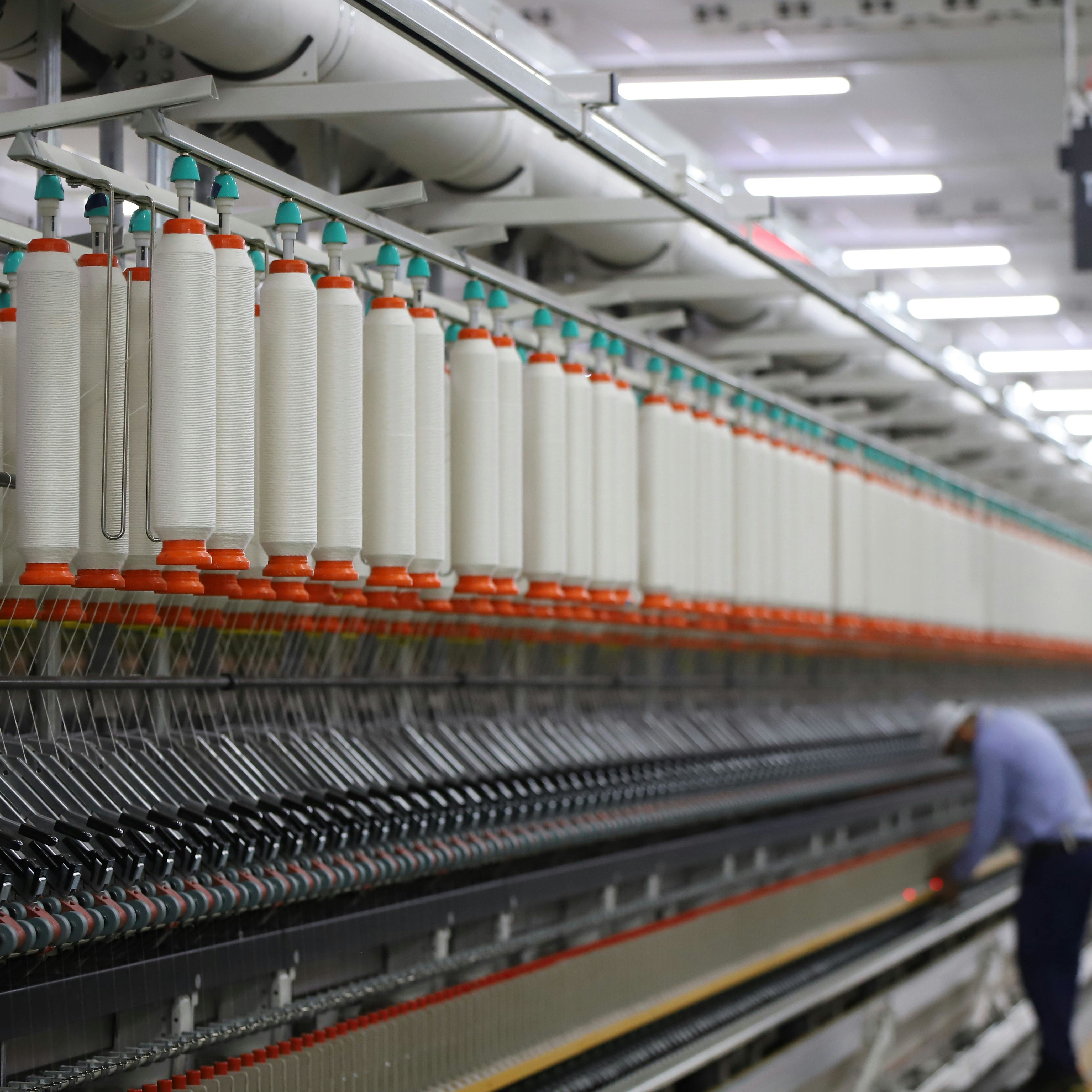 White yarn being spun on industrial spinning machinery.